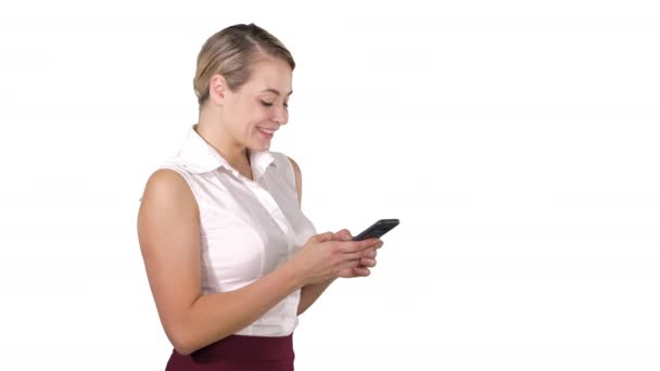 Texting to friend Attractive young woman holding smart phone and looking at it with smile while standing on white background. — Stock Video