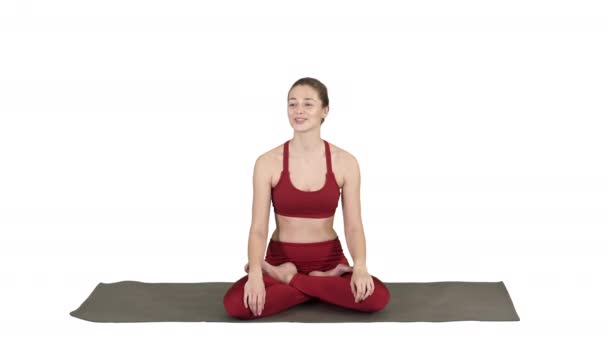 Belle femme assise sur un tapis de yoga et parlant à quelqu'un sur fond blanc. — Video