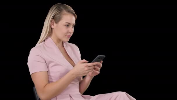 Lächelnde blonde Frau sitzt und nutzt Smartphone, Alpha Channel — Stockvideo