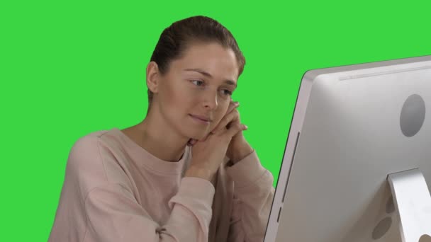 Ξανθιά κορίτσι με ροζ πουλόβερ κοιτάζοντας την οθόνη του υπολογιστή βλέποντας βίντεο σε μια πράσινη οθόνη, πλήκτρο αποχρώσεων. — Αρχείο Βίντεο