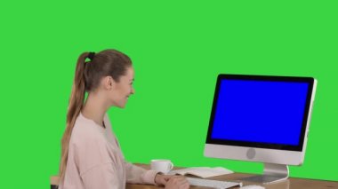Kız bilgisayar monitörün önünde oturan ve bir şeyi izlerken bir yeşil ekran, Chroma anahtar mavi ekran mock-up ekran gülümseyen.