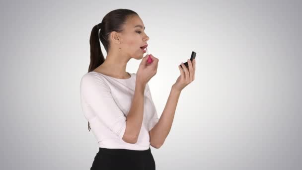 Hermosa mujer, se tiñe los labios de lápiz labial de color rosa, mirando en el espejo sobre fondo degradado. — Vídeos de Stock