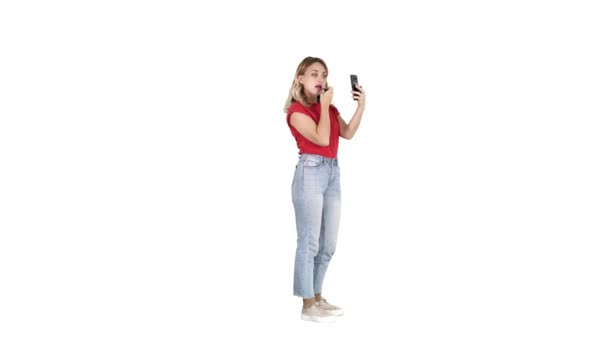 Mulher usando batom e olhando em seu telefone no fundo branco . — Vídeo de Stock
