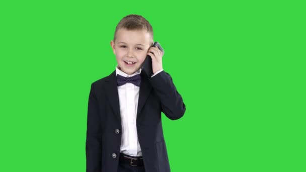 Kleine jongen in een kostuum het maken van een telefoontje tijdens het lopen op een groen scherm, Chroma Key. — Stockvideo