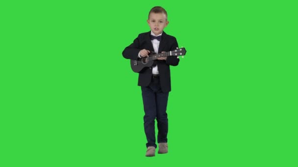 Αγόρι σε ένα κοστούμι περπάτημα και παίζοντας γιουκαλίλι σε μια πράσινη οθόνη, πλήκτρο αποχρώσεων. — Αρχείο Βίντεο