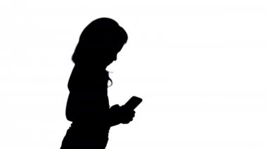 Siluet Küçük kız yürürken akıllı telefon ile oynuyor.