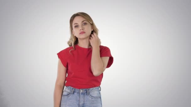 Giovane donna con i capelli biondi in rosso T-shirt guardando la fotocamera senza emozioni su sfondo sfumato . — Video Stock