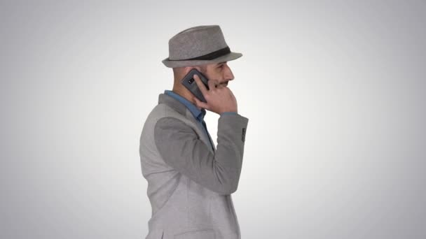Arabski człowiek w przypadkowym chodzeniu i wykonywanie połączenia telefonicznego na tle gradientu. — Wideo stockowe