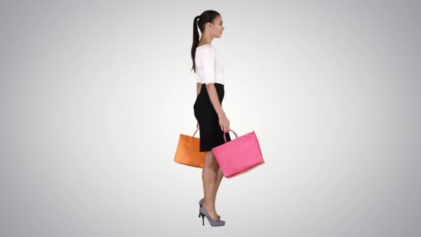 Jonge vrouw met boodschappentassen lopen uit de winkel op gradiënt achtergrond. — Stockvideo