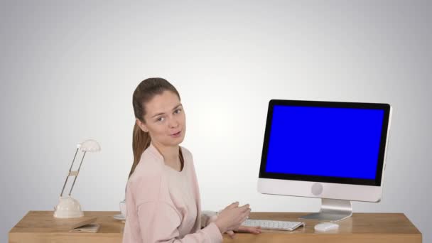 Γοητευτική γυναίκα παρουσιάζοντας κάτι στην οθόνη του υπολογιστή μιλώντας με την κάμερα μπλε οθόνη μακέτα οθόνη στο φόντο ντεγκραντέ. — Αρχείο Βίντεο