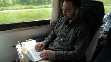 Kulaklık takan genç bir uzman trende dizüstü bilgisayar kullanarak işvereniyle görüntülü konuşma yapıyor..