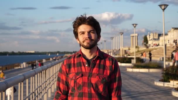 Feliz, joven hombre casual caminando por el paseo marítimo mirando a su alrededor. — Vídeos de Stock