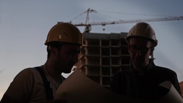 Engineering team is meeting and planning construction work at sunset. One of them smokes. — Stock Video