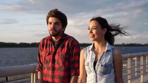Молодий чоловік і жінка насолоджуються сонячним днем, прогулюючись біля річки, розмовляючи і сміючись . — стокове відео