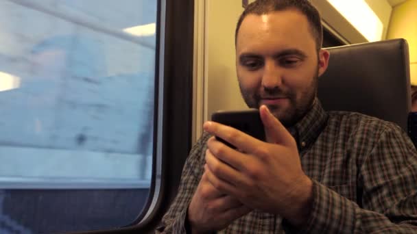 地下鉄の電車に座ってウェブでサーフィンするハンサムな男と彼のスマートフォン. — ストック動画