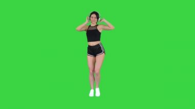 Genç, mutlu, sportif bir kadın kulaklıkla müzik dinliyor ve yeşil ekranda dans ediyor, Chroma Key.