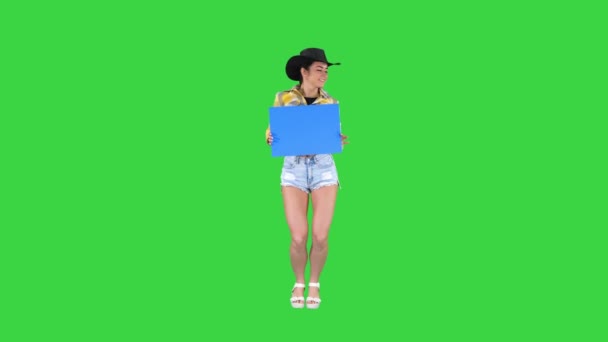Jolie cow-girl souriante tenant une planche vide et dansant sur un écran vert, maquette bleue . — Video