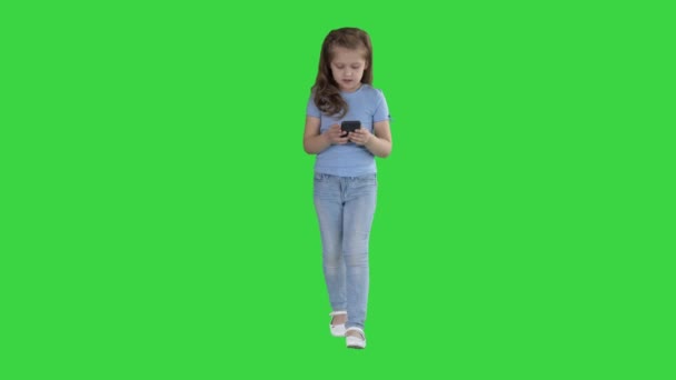Klein schattig meisje verrast met een interessante informatie op een mobiele smartphone op een groen scherm, Chroma Key. — Stockvideo