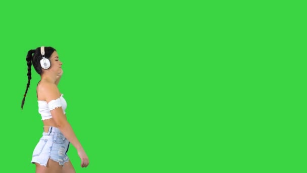 Latin woman with black hair enjoying music in headphones and walking on a Green Screen, Chroma Key. — Stock Video