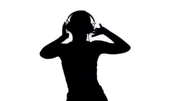 Silhouette Young happy sportive woman listening music in headphones and dancing. — Stock Video