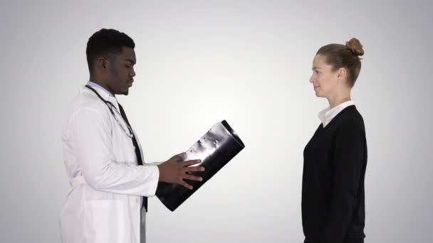 Pacient přijde k doktorovi s rentgenem Fyzioterapeutistou, který vysvětluje rentgen pacienta na pozadí gradientu. — Stock video