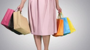 Her gün alışveriş yapan genç bir kadın, arka planda yürürken alışveriş torbaları taşıyor..