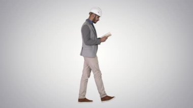 Degrade arka planda yürürken genç mimar okuma ders kitabı veya Notebook.