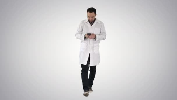 Doctor walking and writing a message on the phone on gradient background. — Stock Video