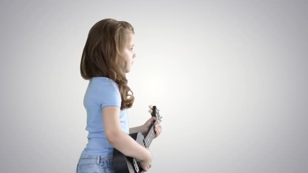 A little girl walking with ukulele in hands on gradient background. — Stock Video