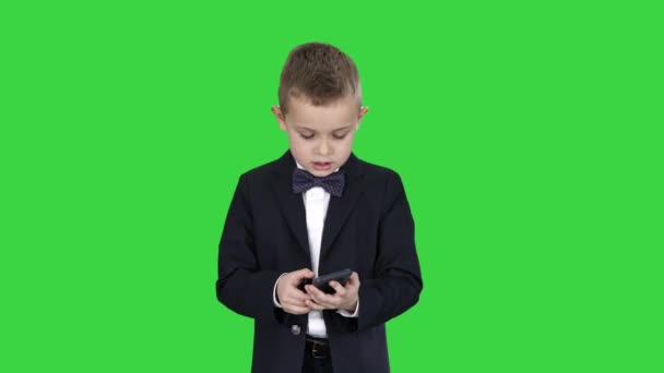 Liten pojke i kostym gå och använda smartphone på en grön skärm, Chroma Key. — Stockvideo