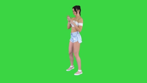 Söt tjej kollar sin mobil och dansar på en grön skärm, Chroma Key. — Stockvideo