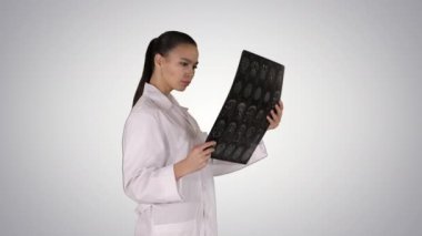 Beyaz önlüklü entellektüel kadın sağlık personeli röntgen görüntülerine, tomografiye, gradyan arka planda MRI 'ya bakıyor..