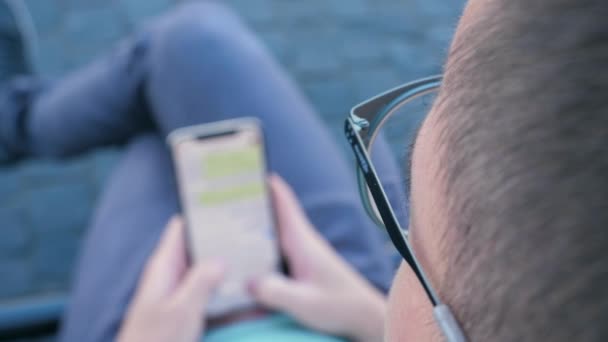 Man using his smartphone writing a message sitting on a bench. — Stock Video