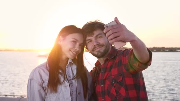 El atractivo hombre casual y una mujer tomando una selfie con una puesta de sol. — Vídeos de Stock