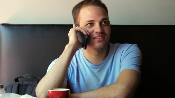 Inquadratura interna di giovane uomo sorridente seduto e parlando sul telefono cellulare. Felice giovane ragazzo al caffè parlando al telefono. — Video Stock