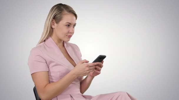 Gülümseyen sarışın kadın, arka planda oturuyor ve akıllı telefon kullanıyor.. — Stok video
