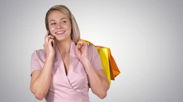 Jeune femme avec des sacs à provisions parlant sur téléphone mobile sur fond de dégradé . — Video