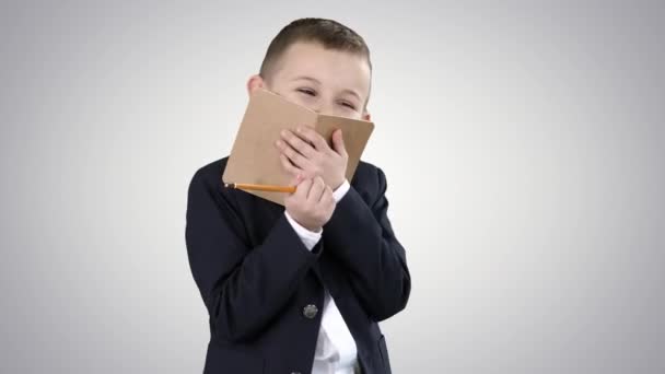 Emotionele positieve kleine jongen met notebook lachen op gradiënt achtergrond. — Stockvideo