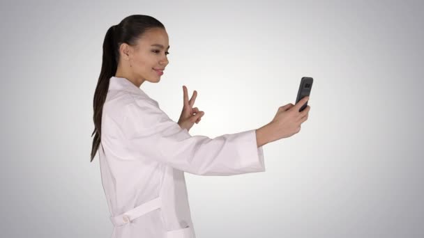 Elegante medico europeo bruna che prende selfie al telefono mentre cammina su sfondo sfumato. — Video Stock