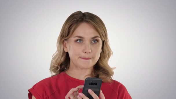 Pensando rubia bonita enviando un mensaje de texto en su teléfono en un fondo degradado. — Vídeo de stock