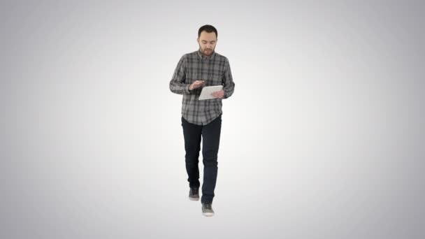 Sonriente hombre con la tableta caminando y hablando con la cámara en el fondo gradiente . — Vídeos de Stock