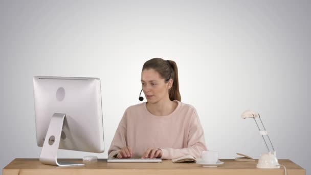 Красивая молодая случайная женщина в наушниках работает на компьютере на градиентном фоне. — стоковое видео