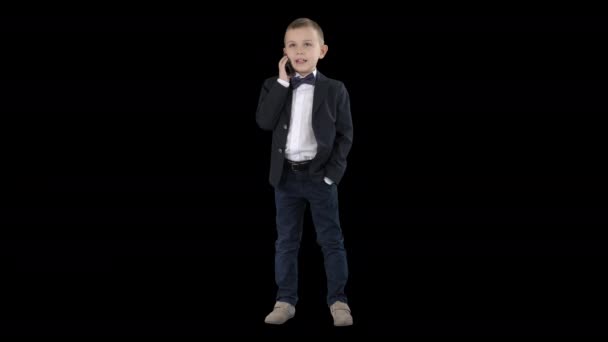 Söt liten pojke talar på sin smartphone och stående i en mörk kostym, alfakanal — Stockvideo