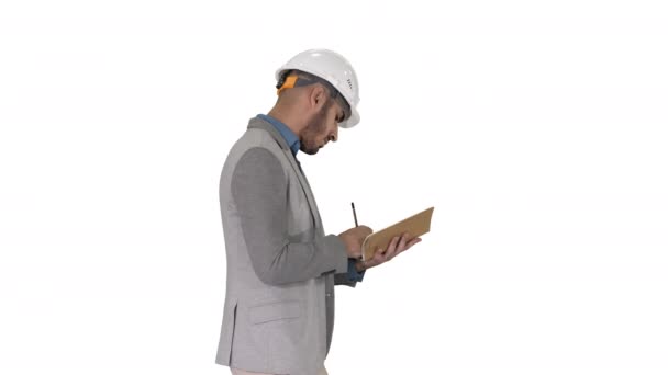 Hombre árabe en ropa casual y sombrero duro anotando lista de verificación sobre fondo blanco. — Vídeo de stock