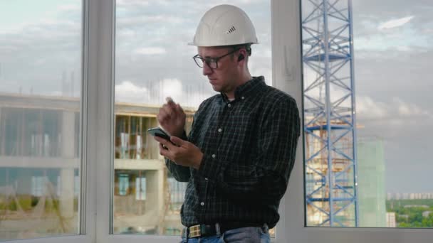 Constructeur of ingenieur luisteren muziek op koptelefoon van zijn telefoon tijdens de pauze. — Stockvideo