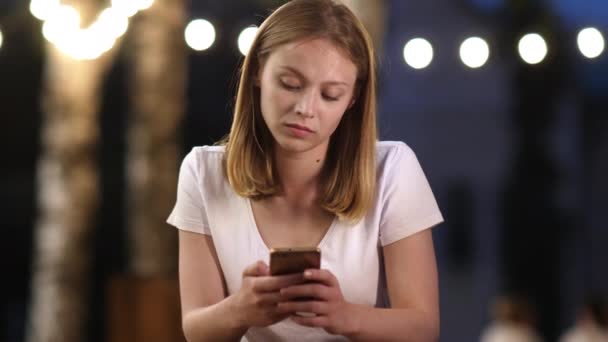 Cheerless triste attraente ragazza nervosa digitando messaggio seduto nel parco in serata. — Video Stock