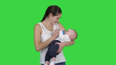 Anne yeşil ekranda şişeden içmek için bebek verir, Chroma Anahtar.