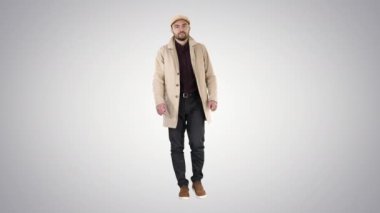Açık trençkot lacivert sakallı adam degrade arka planda yürüyor.
