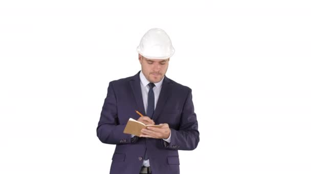 Инженер в костюме и шлеме ходит и пишет заметки в блокноте на белом фоне. — стоковое видео