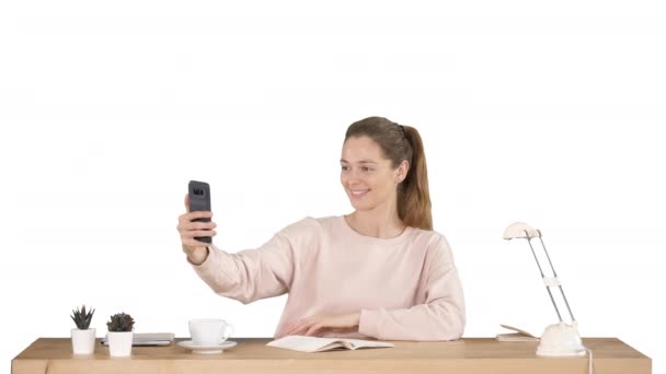 Mulher bonita tirando uma selfie com seu telefone celular sentado na mesa no fundo branco. — Vídeo de Stock